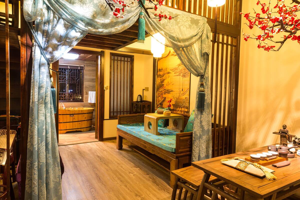 Una habitación tradicional con una cama de madera, una mesita con juego de té y un cuadro grande en la pared.