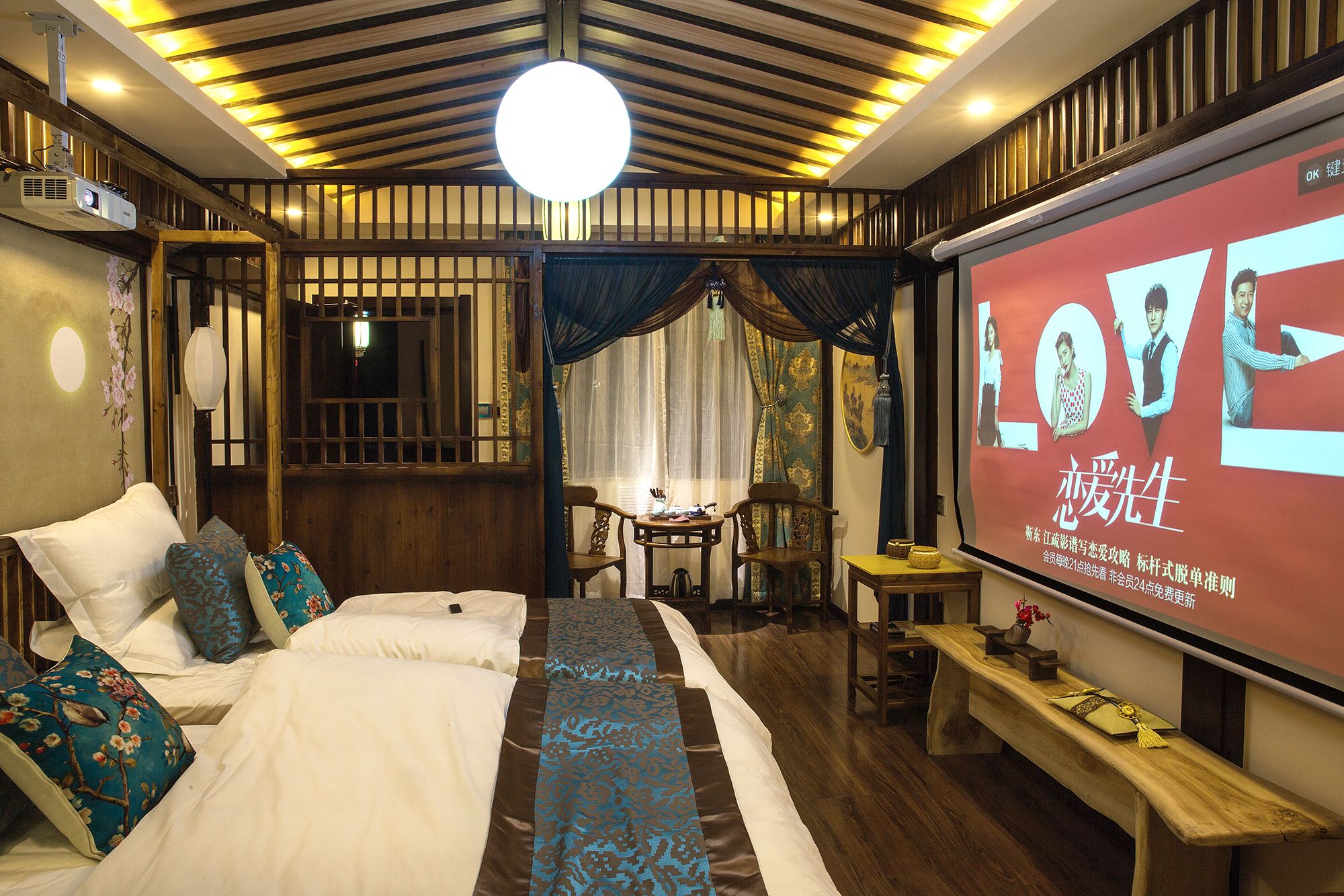 A traditional-style bedroom with a bed, pillows, a desk, and a screen displaying a movie.