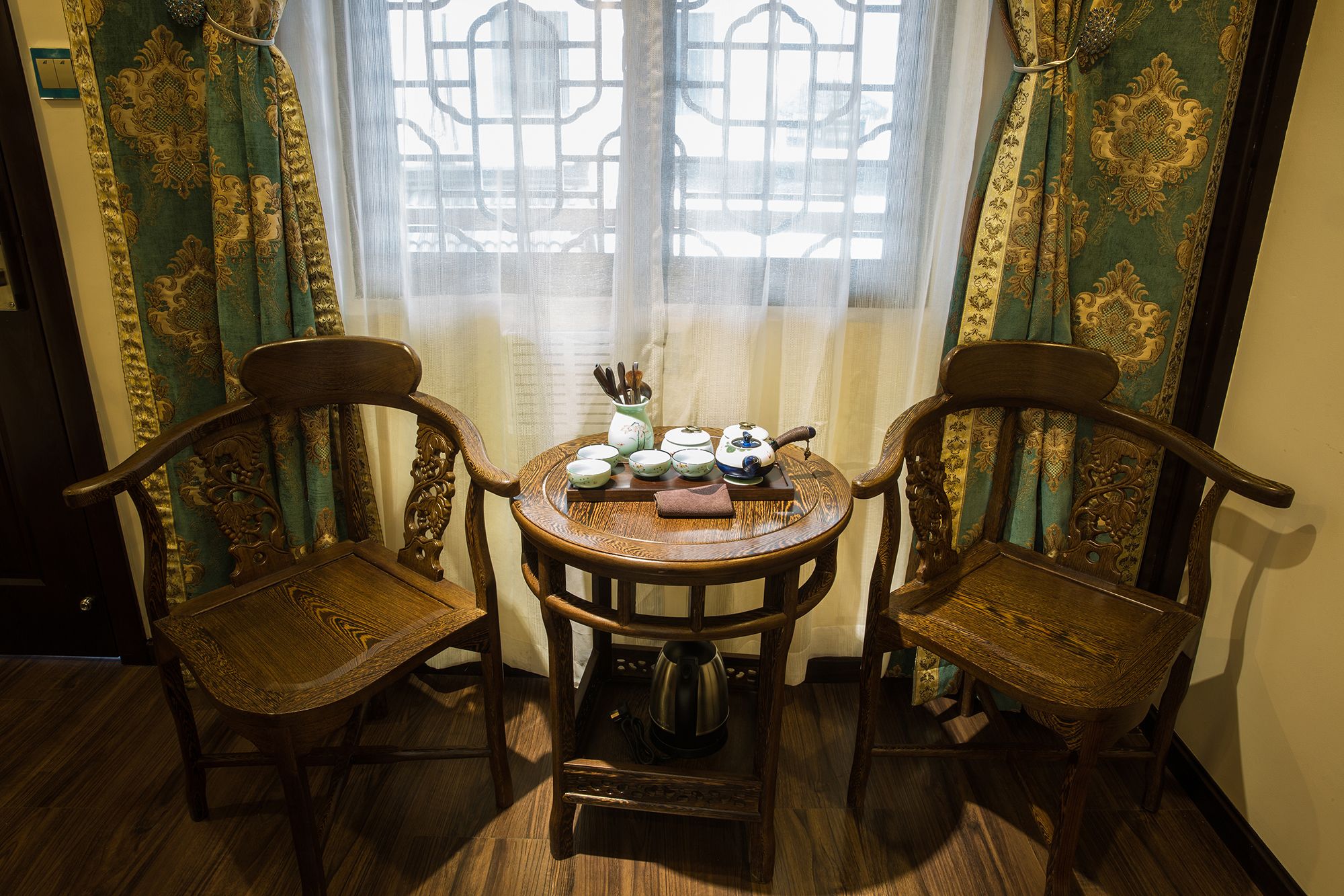 A traditional room with two wooden chairs, a small round table, and a window with decorative curtains.