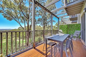 A wooden deck with a table and chairs, overlooking a grassy area with trees. - Tranquility 3br Villa within Cypress Lakes Resort (Pokolbin)