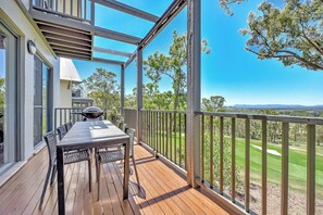 A wooden deck with a table and chairs, overlooking a golf course.