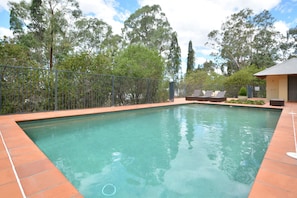 A rectangular swimming pool with a tiled edge, surrounded by a metal fence, and trees in the background.