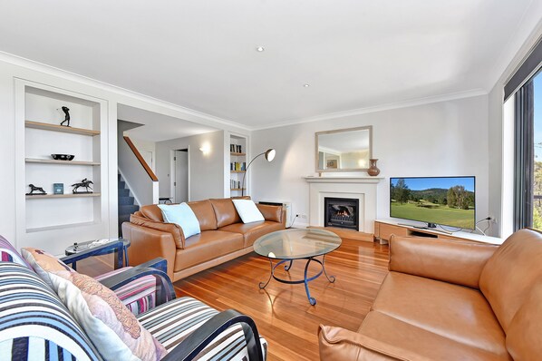 A modern living room with a leather sofa, a glass coffee table, a fireplace, and a television.