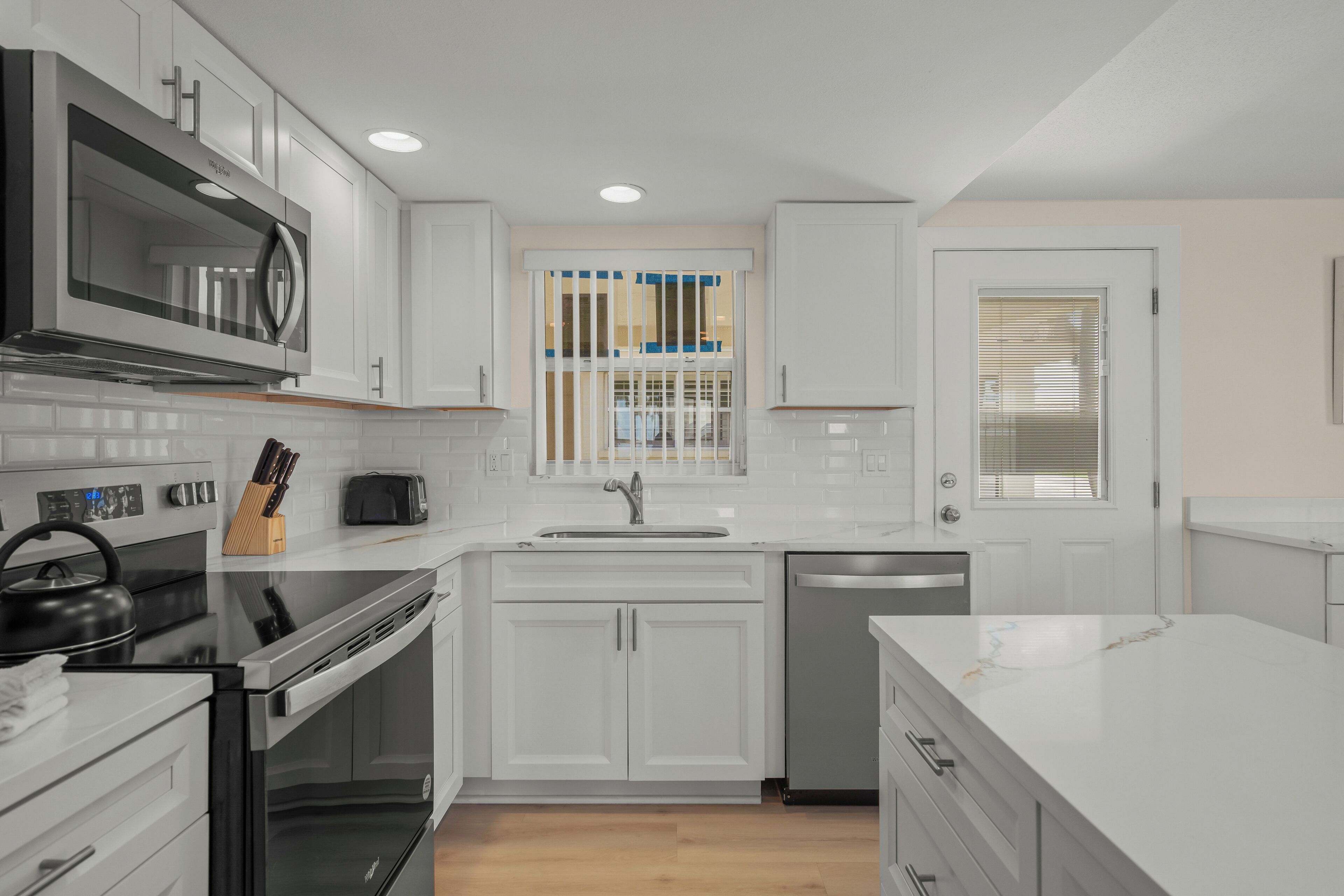 A modern kitchen with white cabinets, a stainless steel microwave, a stove, and a dishwasher.
