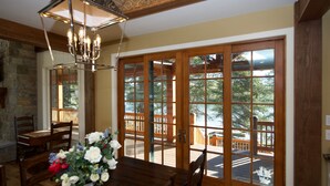 A dining area with a wooden table and chairs, a vase with flowers, and large glass doors leading to an outdoor deck.