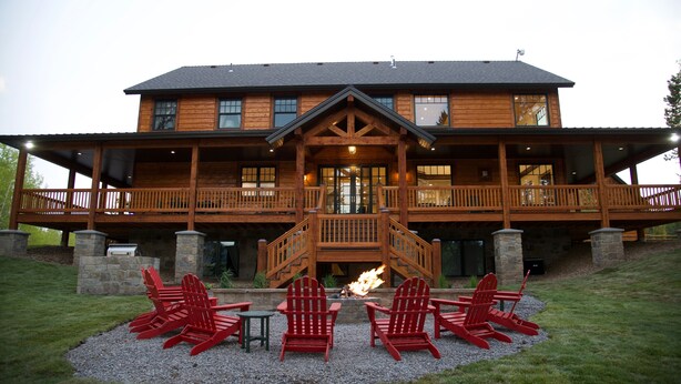 A large wooden lodge with a covered deck and outdoor seating area.