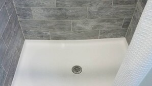 A shower with a drain in the center, surrounded by gray stone tiles. - Studio Apt by beach - unit #14 (Scarborough)