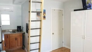 A room with a wooden ladder, a kitchenette, a white wardrobe, and a blue sofa. - Studio Apt by beach - unit #14 (Scarborough)