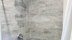 A shower with grey tiles and a metal shower head. - Studio Apt by beach - unit #14 (Scarborough)