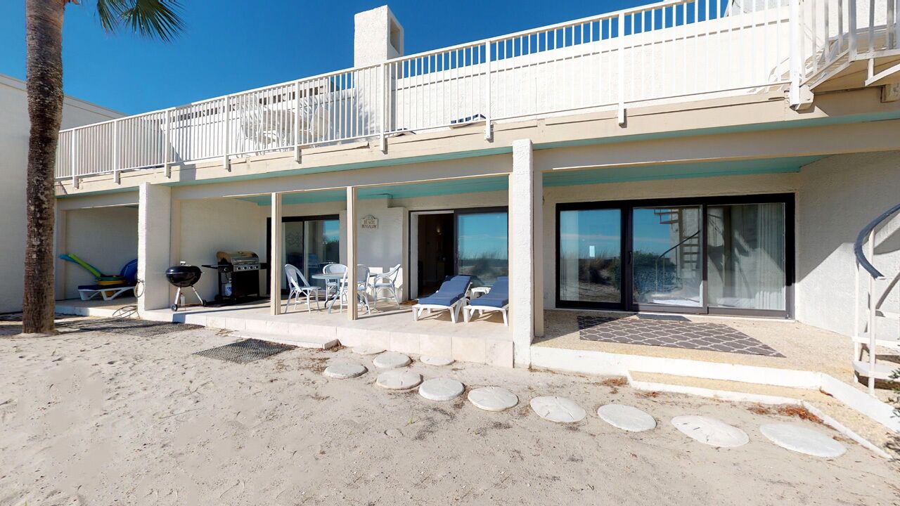 A beachfront property with a covered patio, lounge chairs, and a grill area.