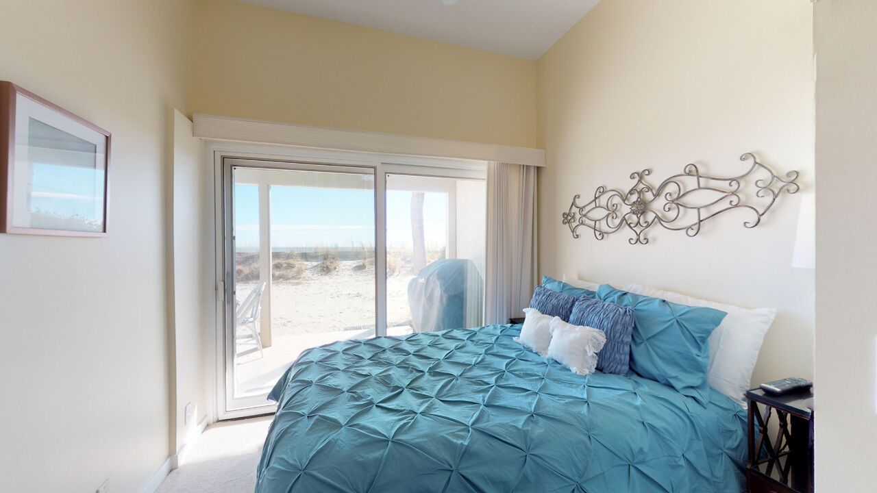 Een slaapkamer met een groot bed, een schuifpui naar het strand en een decoratief wandobject.