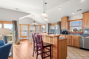 Een moderne keuken met houten kasten, een centraal eiland en een eetgedeelte met stoelen.