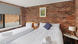 Habitación de hotel con dos camas, pared de ladrillo, ventana con vistas y un cuadro en la pared.