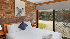 Habitación de hotel con pared de ladrillo, cama grande con ropa de cama blanca, almohada azul y un cuadro enmarcado de un koala.