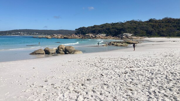 Una playa de arena blanca, agua azul cristalina y rocas grandes al frente.