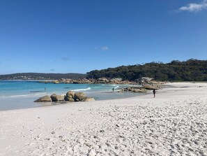 Une plage de sable blanc, avec une eau d’un bleu limpide et de gros rochers au premier plan.