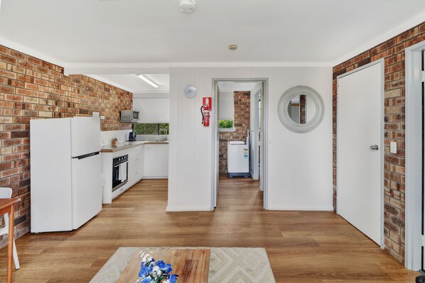 A modern kitchen with white appliances, a brick accent wall, and a wooden floor.
