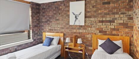 Una habitación de hotel con dos camas individuales, una pared de ladrillo, una ventana con persiana y un cuadro enmarcado sobre las camas.