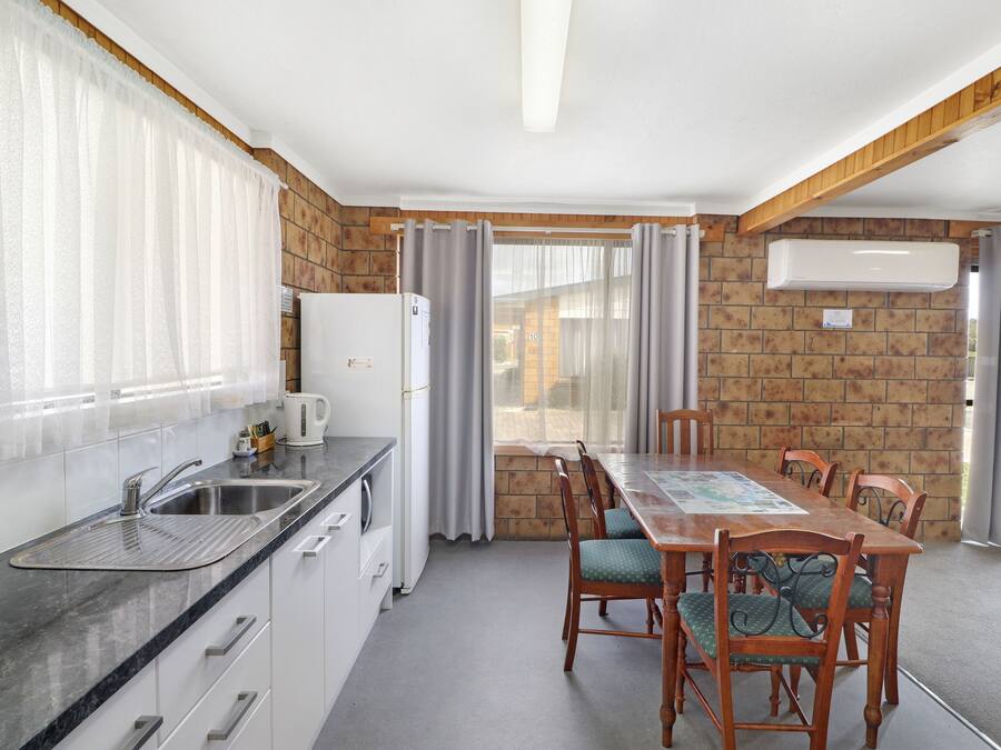 Una cocina con lavamanos, estufa y comedor con sillas y una mesa.