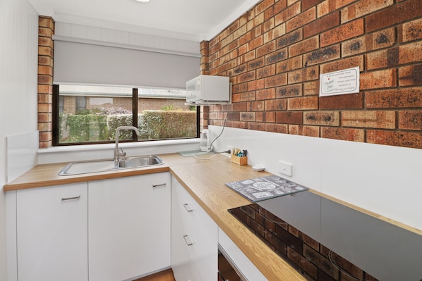 Una cocina moderna con armarios blancos, encimera de madera, estufa empotrada y pared de ladrillo.