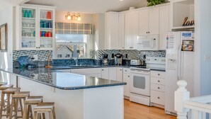 Una cocina moderna con armarios blancos, una isla grande y vista a una casa por la ventana.