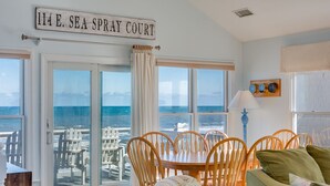 Una habitación con vista al océano, una mesa de comedor con sillas y un letrero que dice "114 E. SEA SPRAY COURT".