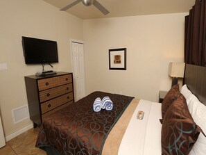 A hotel room with a bed, a TV, a dresser, a framed picture, and a ceiling fan. - Escape to Paradise–The Beach Club AMI #1 by RVA (Bradenton Beach)