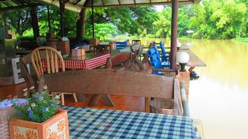 A covered outdoor seating area with a checkered tablecloth, wooden chairs, and a bench.