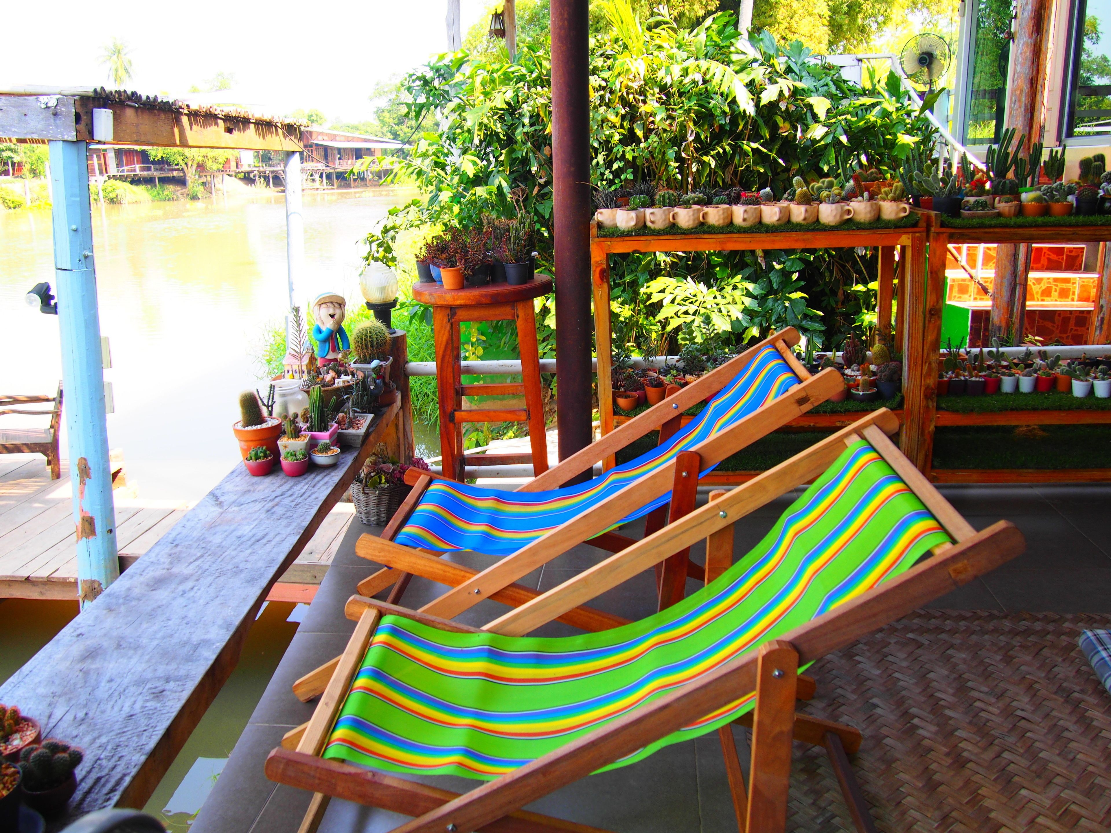 A wooden deck with two striped lounge chairs, a wooden table with potted plants, and a wooden structure with more plants.