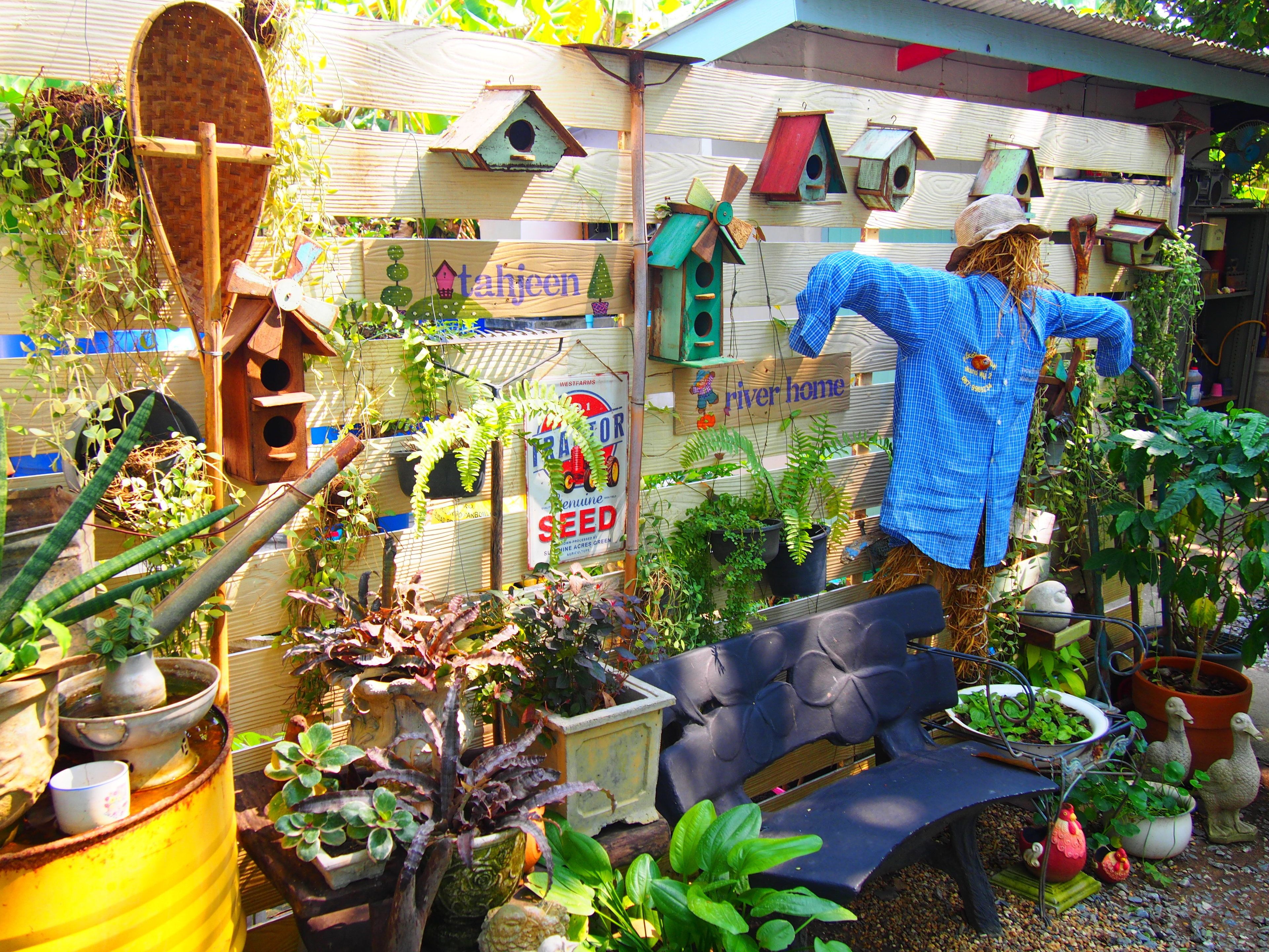 A garden with various potted plants, birdhouses, and a scarecrow figure.