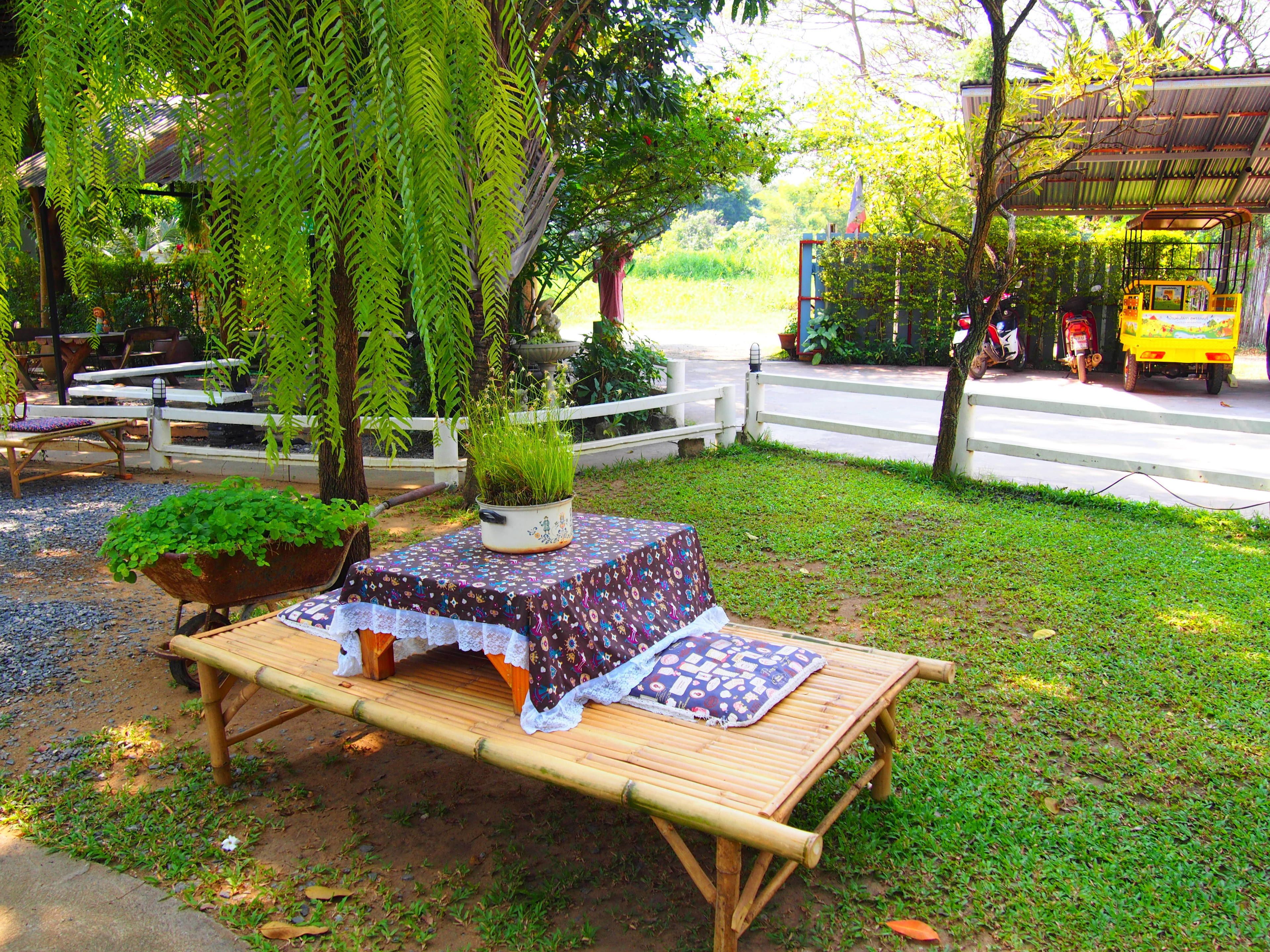 A bamboo table with a patterned tablecloth, surrounded by greenery and a white fence.