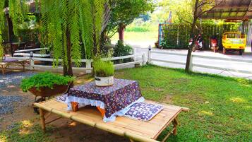 A bamboo table with a patterned tablecloth, surrounded by greenery and a white fence.