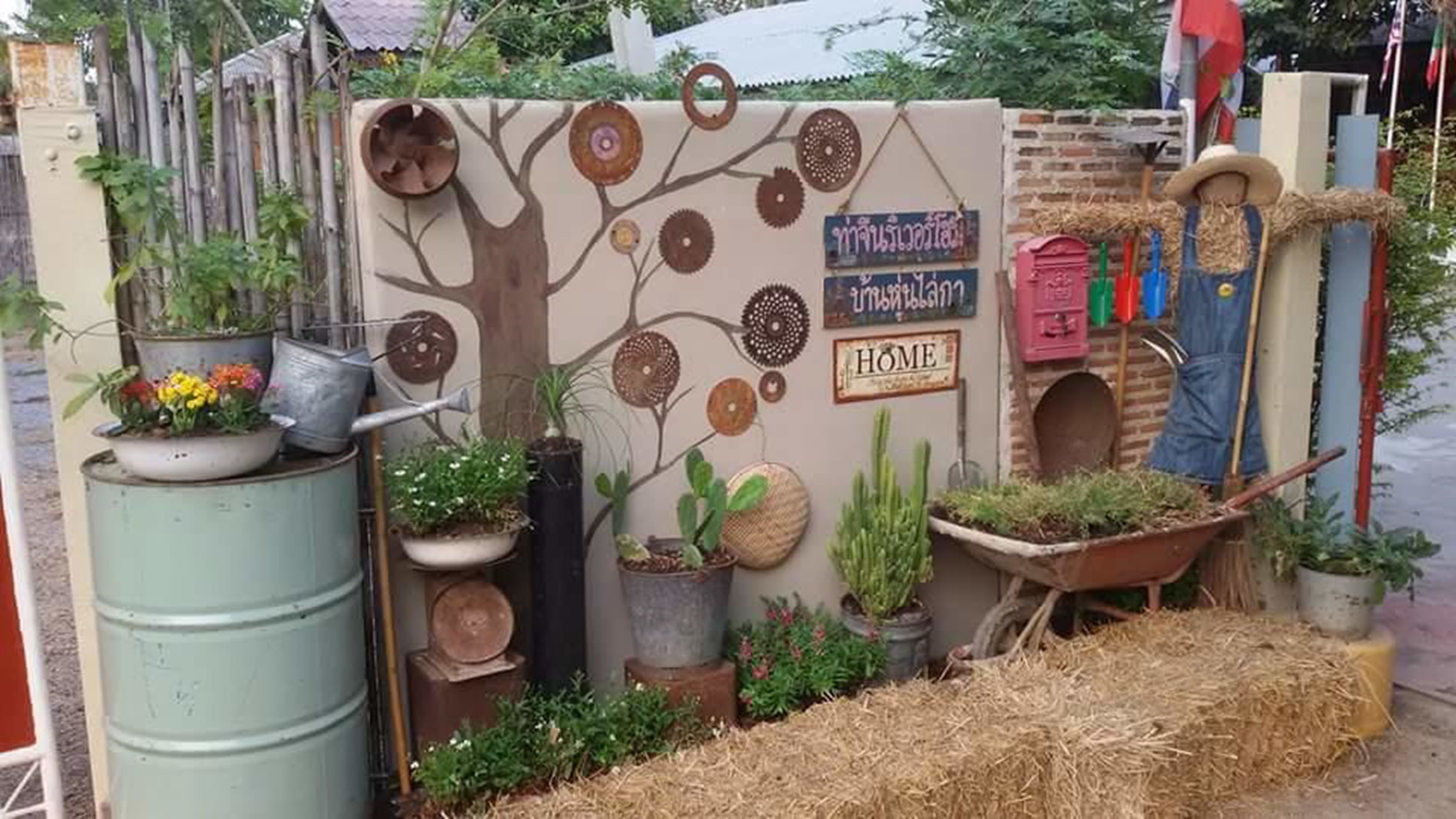 A rustic outdoor display with potted plants, a wheelbarrow, and a tree mural on a wall.