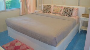 Een slaapkamer met een bed, een nachtkastje, een raam met gordijnen en uitzicht op groen.