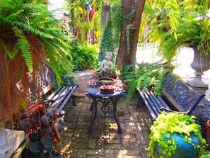 Ein Garten-Terrasse mit zwei Bänken, einer Statue und verschiedenen Kübelpflanzen.