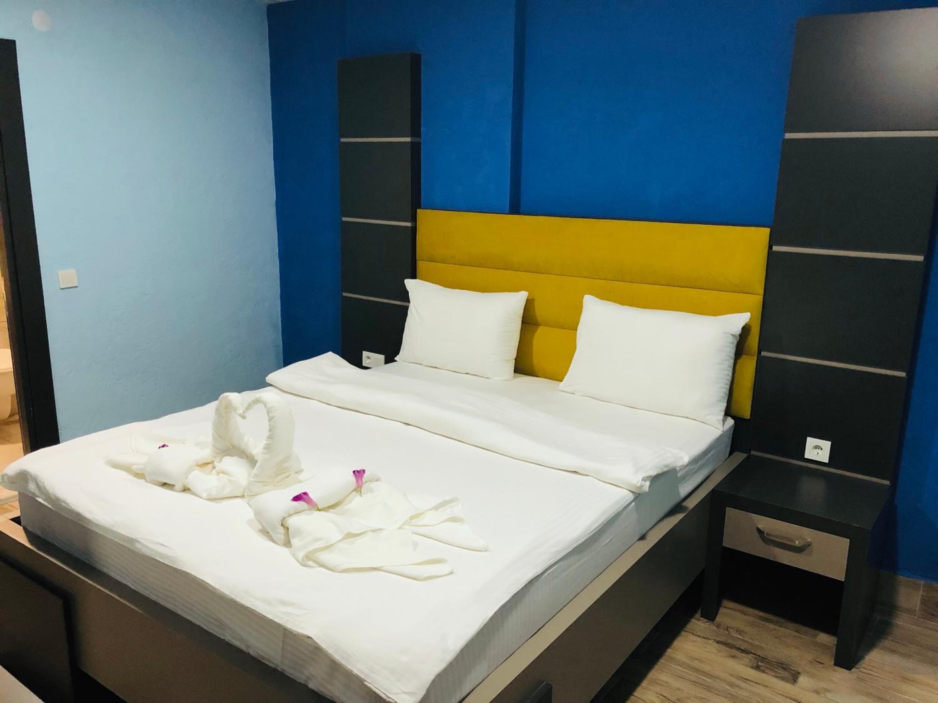 A neatly made bed with white linens and towels, a yellow headboard, and a blue wall.