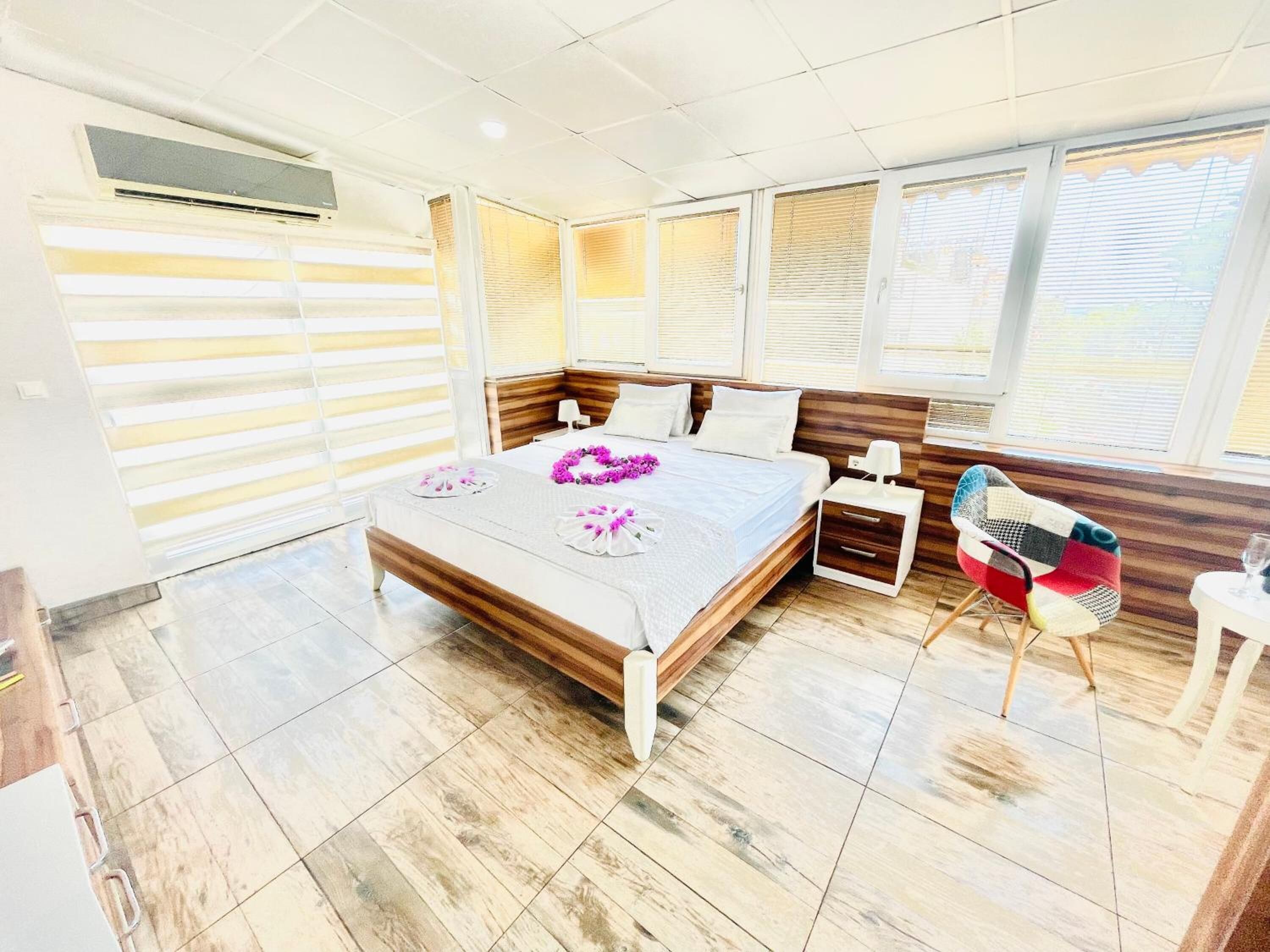 Quarto moderno com uma cama grande, cabeceira de madeira, mesa de cabeceira, uma cadeira e janela com persianas.