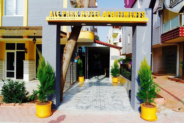 La entrada a Ale Park Hotel Apartments, con un camino despejado que lleva a la entrada, plantas en macetas a ambos lados y un cartel sobre la entrada.