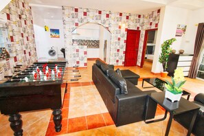 A room with a foosball table, a sofa, a coffee table, and a potted plant.