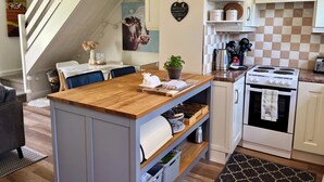 A kitchen with a central island, a stove, and a dining area with a staircase. - Charming, Modern Masonette in Fermoy River Town. Pet Friendly. (Fermoy)