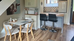 A modern kitchen with white cabinets, a refrigerator, and a dining area with a table and chairs. - Charming, Modern Masonette in Fermoy River Town. Pet Friendly. (Fermoy)