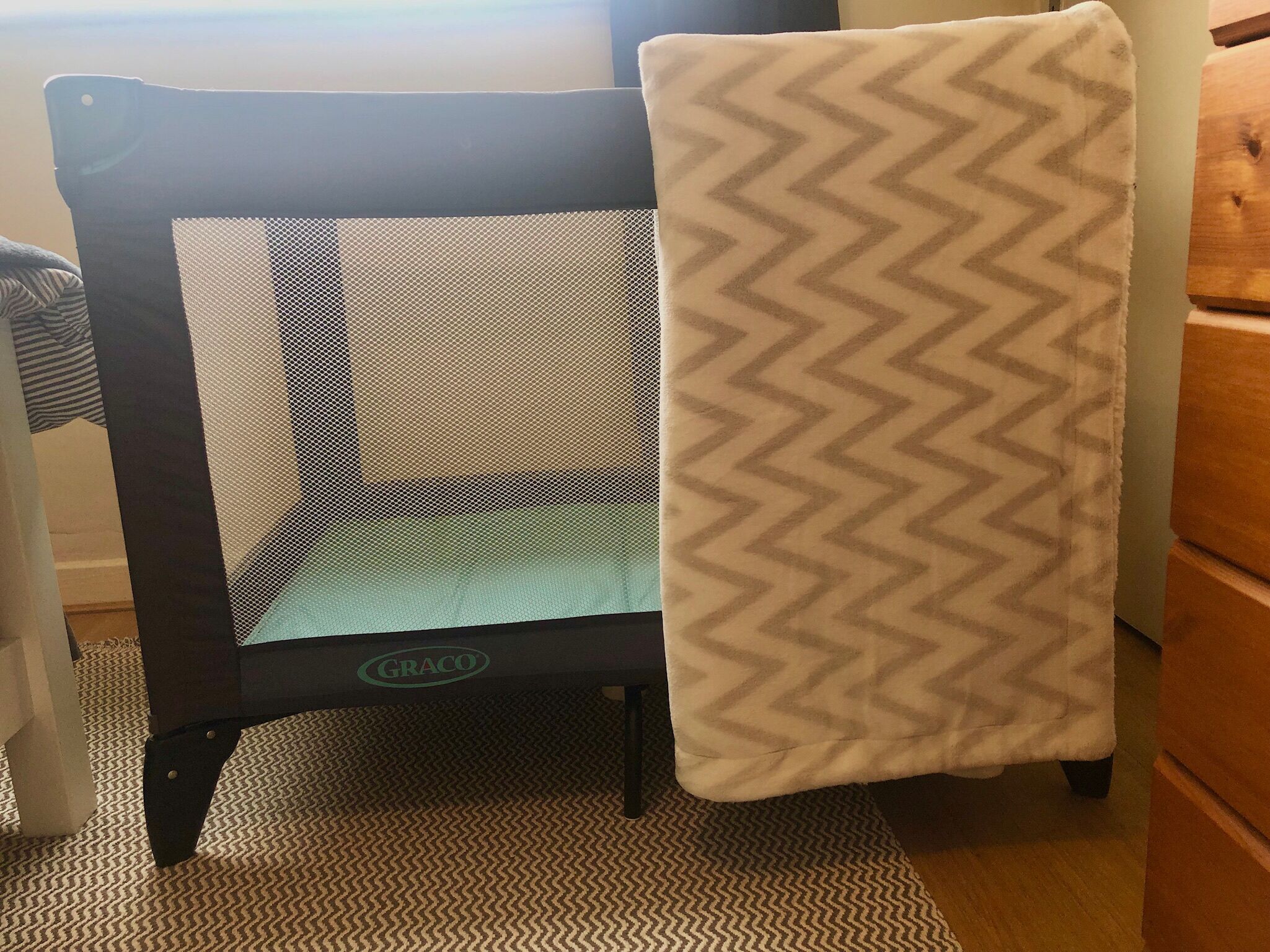A baby playpen with a mesh back and a chevron-patterned cover.