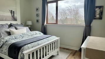 Un dormitorio con cama, mesita de noche, ventana con cortinas y vistas a árboles.