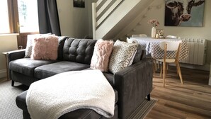 A living room with a dark leather sofa, a white throw blanket, and a staircase leading to an upper level. - Charming, Modern Masonette in Fermoy River Town. Pet Friendly. (Fermoy)