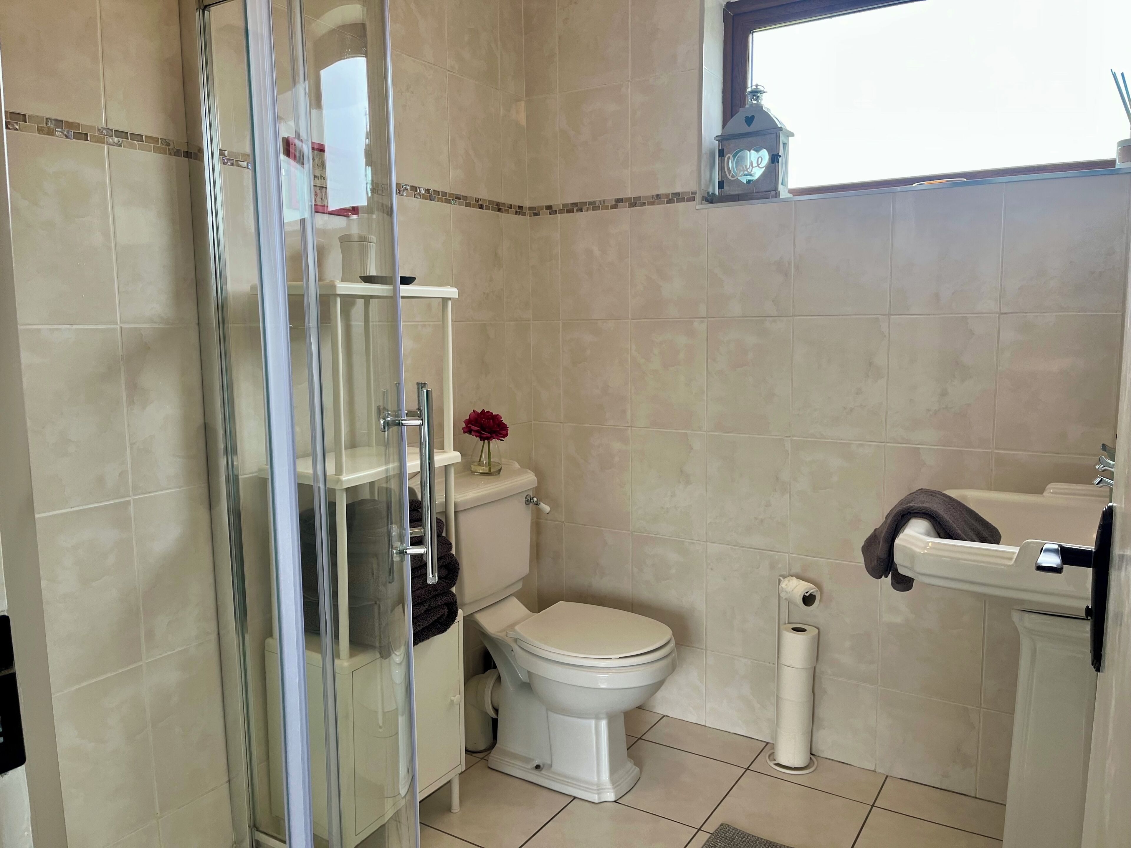 Une salle de bain avec une douche à parois de verre, des toilettes, un lavabo et une fenêtre.