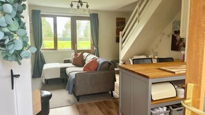 A cozy room with a sofa, a wooden desk, a staircase, and a view of greenery outside. - Charming, Modern Masonette in Fermoy River Town. Pet Friendly. (Fermoy)