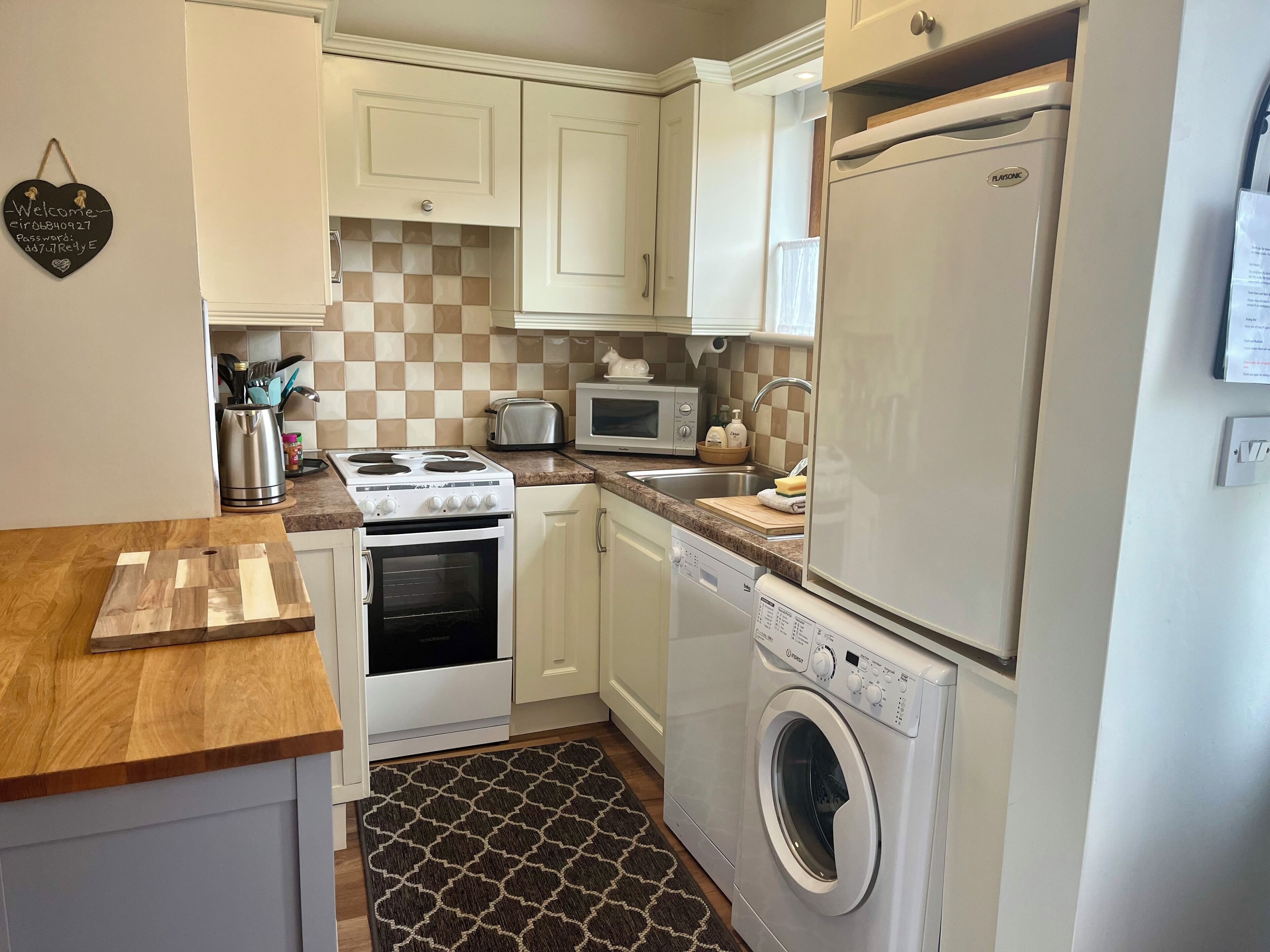 A compact kitchen with white cabinets, a microwave, a toaster, a stove, a dishwasher, and a washing machine.