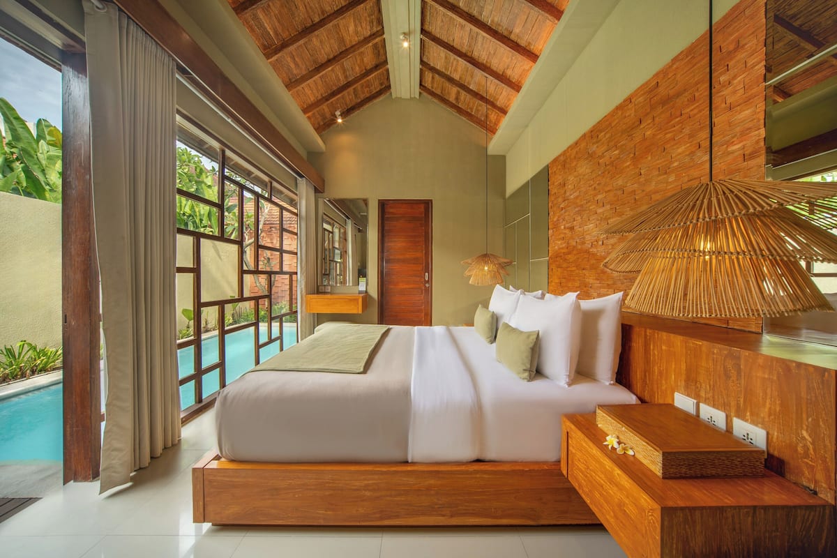 A bedroom with a large bed, a wooden headboard, a bedside table, and a view of a swimming pool.