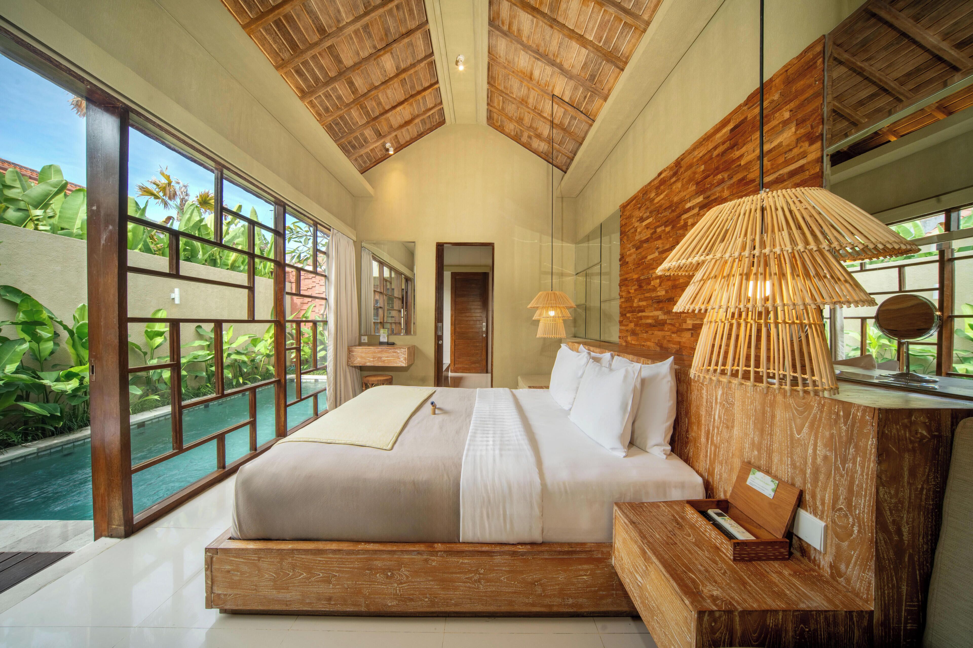 A spacious bedroom with a large bed, a wooden headboard, a bedside table, and a view of a swimming pool.