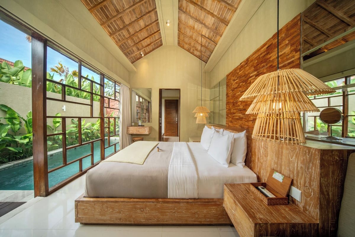 A spacious bedroom with a large bed, wooden headboard, and a view of a swimming pool.